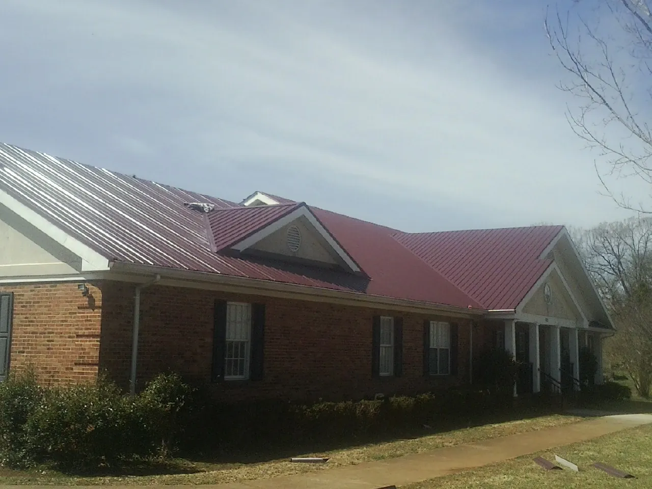 Red metal roof with gabled entries on a long brick building, from a Hail Damage Roof Repair job in Hays