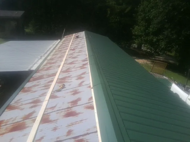 Old rusted panels beside newly installed green metal roofing — Wind Damage Roof Repair by Roofing Brothers in Hays