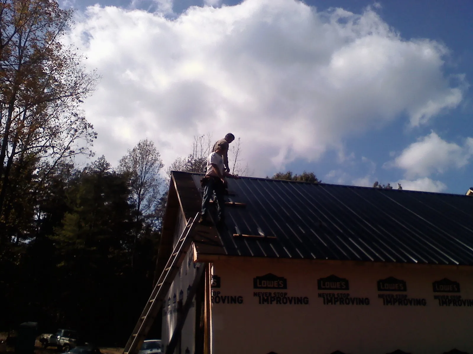 Roofer fastening dark metal panels high against a cloudy sky, from a Roof Inspection job in Hays