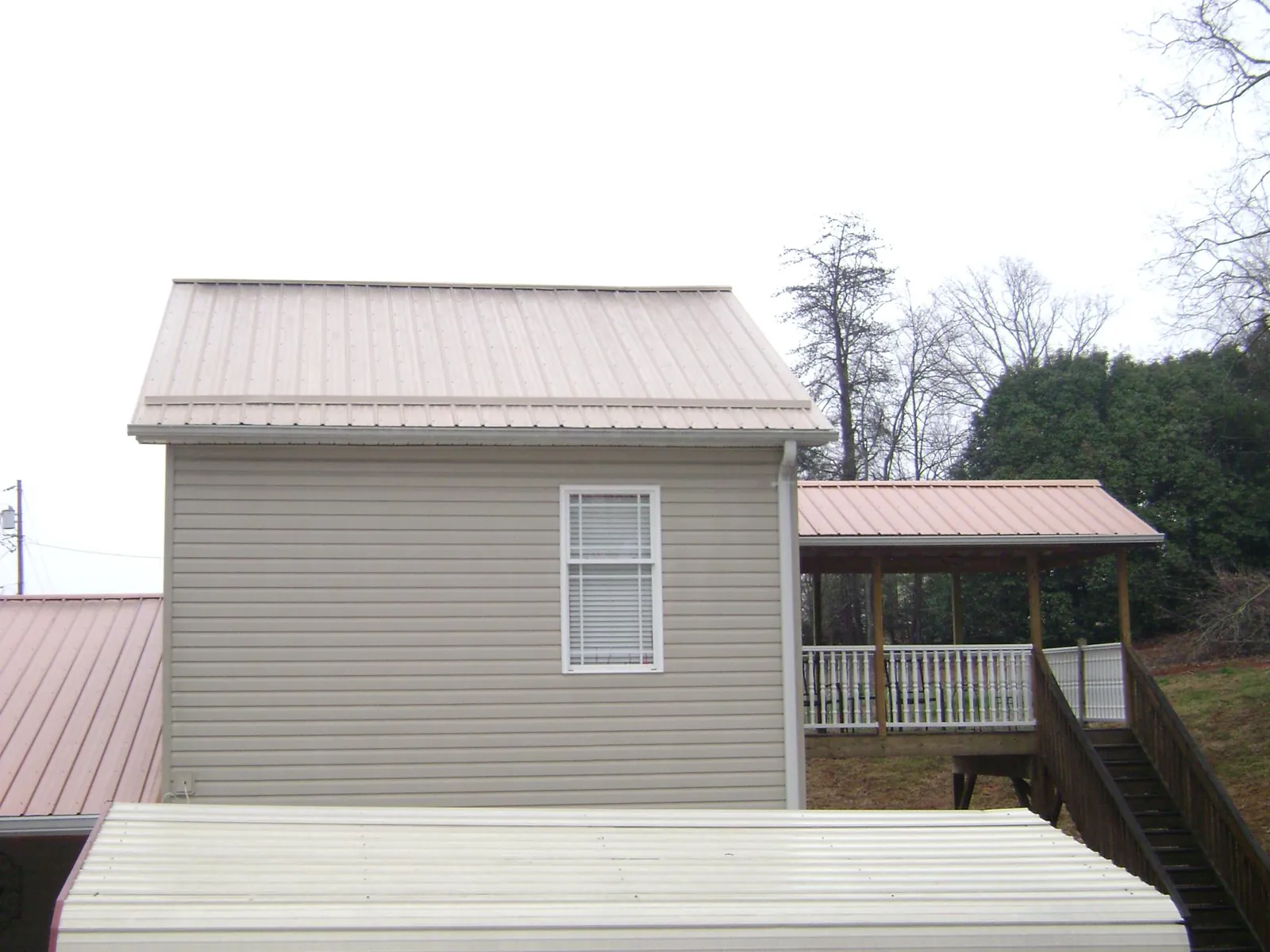 Tan metal roofs on a two story addition and attached porch, from a Roof Replacement job in Hays
